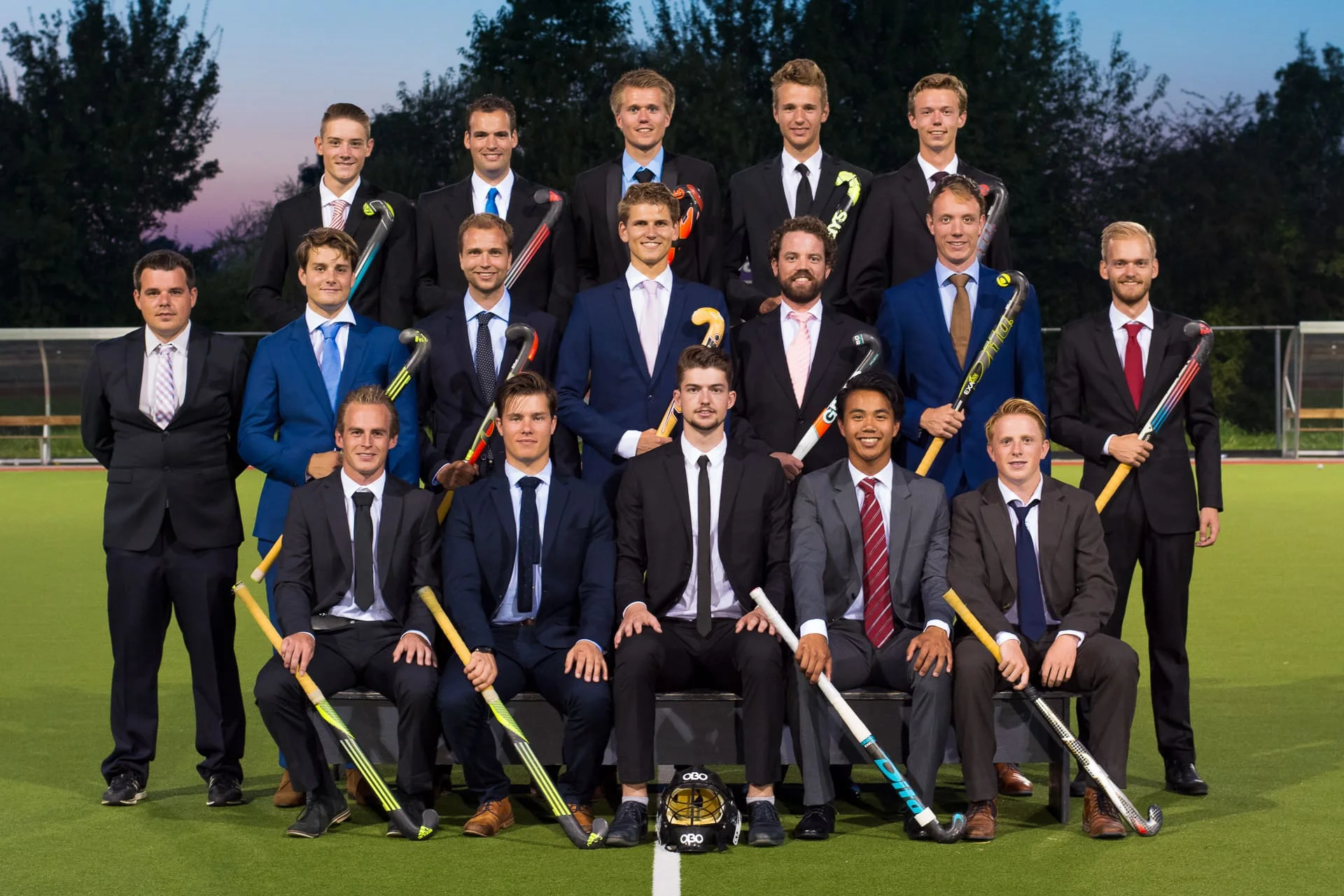 Teamfoto van MHC de Westerduiven Heren 1 in een tweedelig pak en hockeystick, Seizoen 2016 - 2017