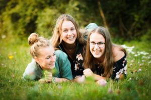 Vriendenfoto van Merel, Fleur en Roos die in het gras liggen en de grootste lol hebben met elkaar.