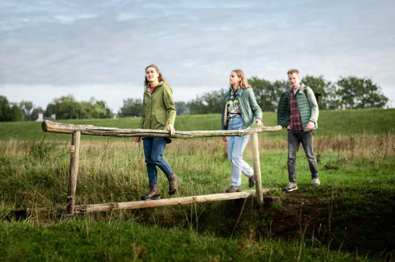 3 personen lopen over het bruggetje van het klompenpad.