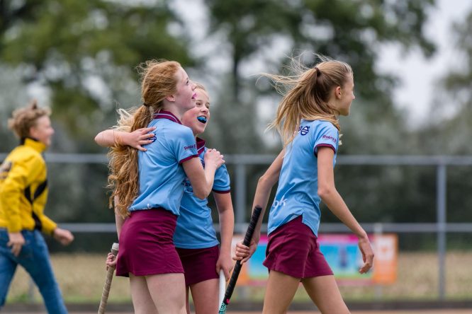 Jonge hockeyspeelster geeft een schouderklop aan een mede speler voor het maken van een doelpunt.